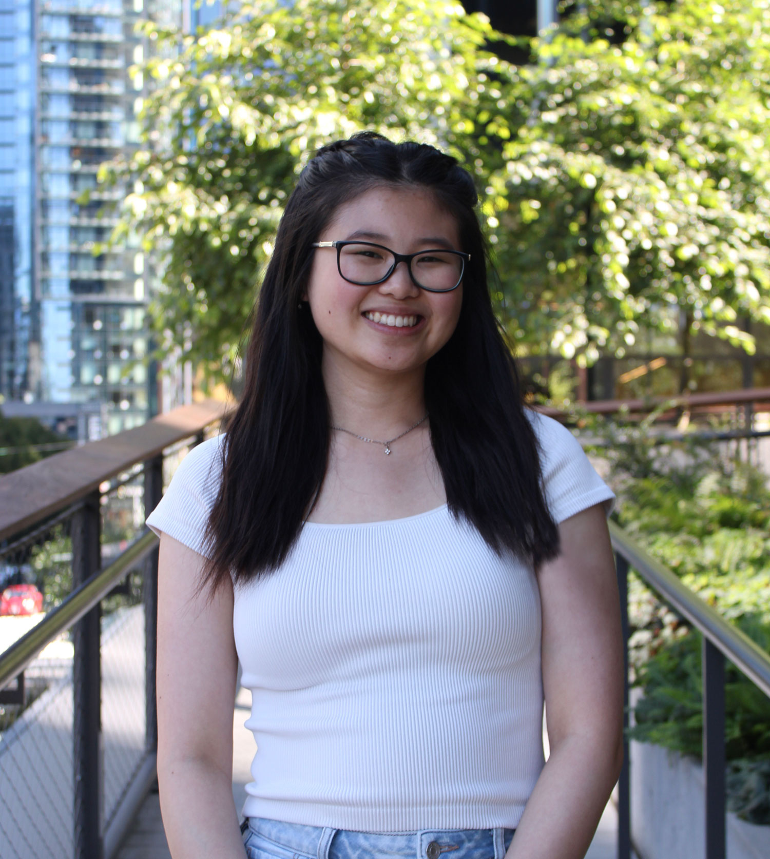 Portrait of Carmen standing outside, smiling and dressed casually in natural lighting.