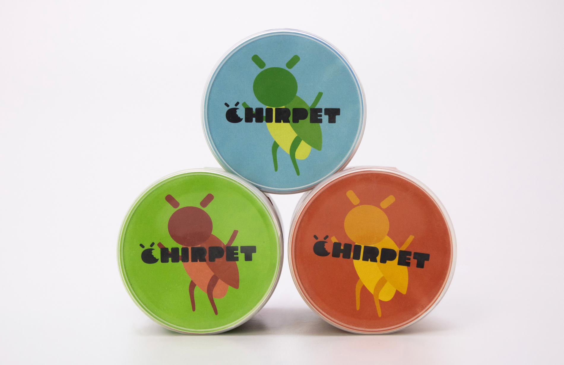 View of the lids balanced on top of each other in a prism shape, showcasing the top view of the Chirpet cans: a cricket illustration and the Chirpet logo.