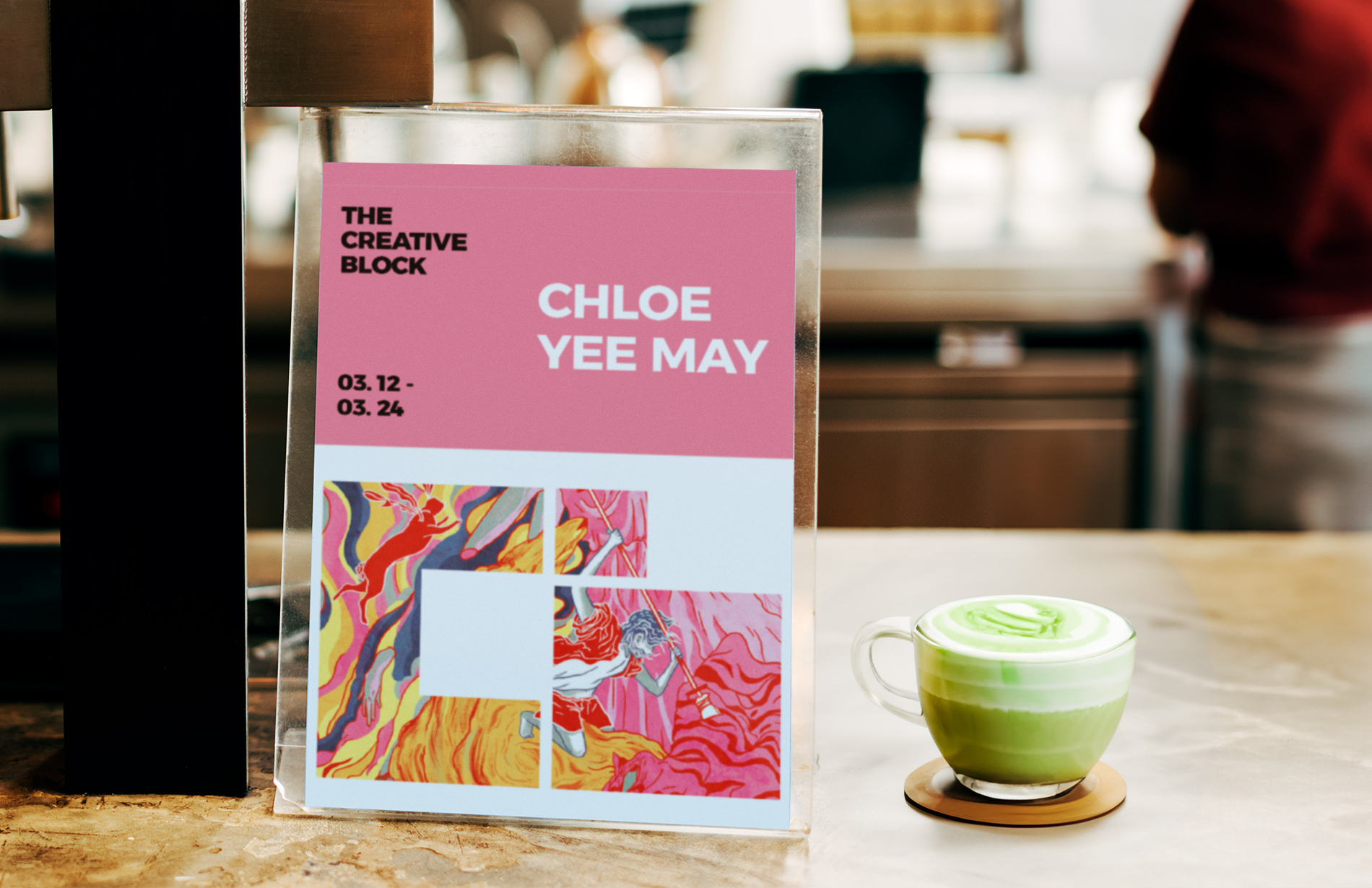 Poster showcasing featured artwork by Chloe Yee May with The Creative Block branding, inside a poster stand on a countertop inside cafe setting. Next to it is a matcha latte. 